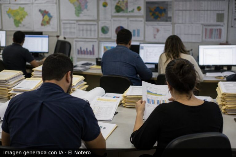 Interior de una oficina de encuestas con personas de espaldas revisando gráficos y carpetas, en un ambiente de trabajo periodístico.