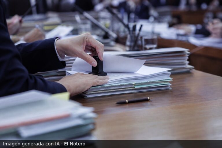 Primer plano de manos anónimas revisando y sellando expedientes laborales sobre una mesa de trabajo, con figuras desenfocadas al fondo.
