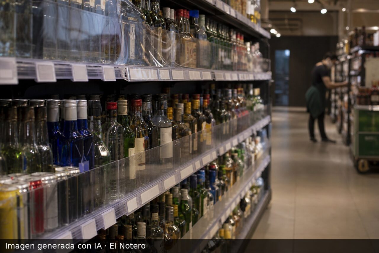 Estantes de supermercado con bebidas alcohólicas parcialmente restringidas y sectores vacíos, con un empleado desenfocado al fondo.