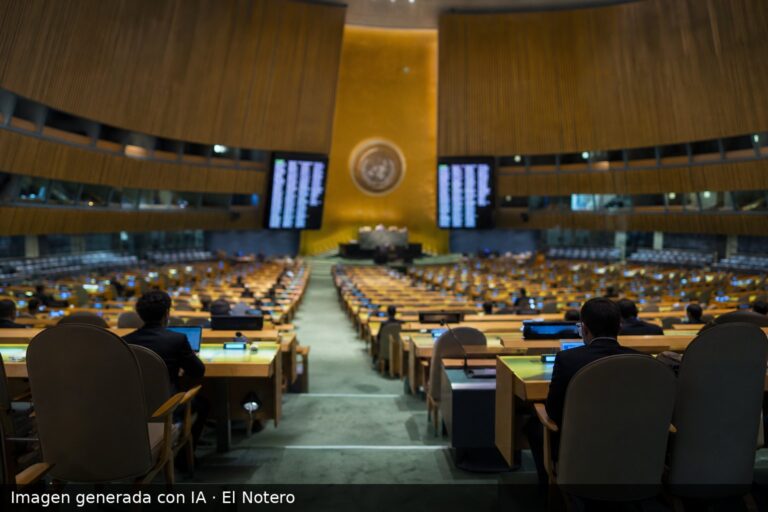 Vista amplia del recinto de la Asamblea General de la ONU desde el fondo, con filas de asientos vacíos y algunos delegados anónimos desenfocados bajo luz fría.